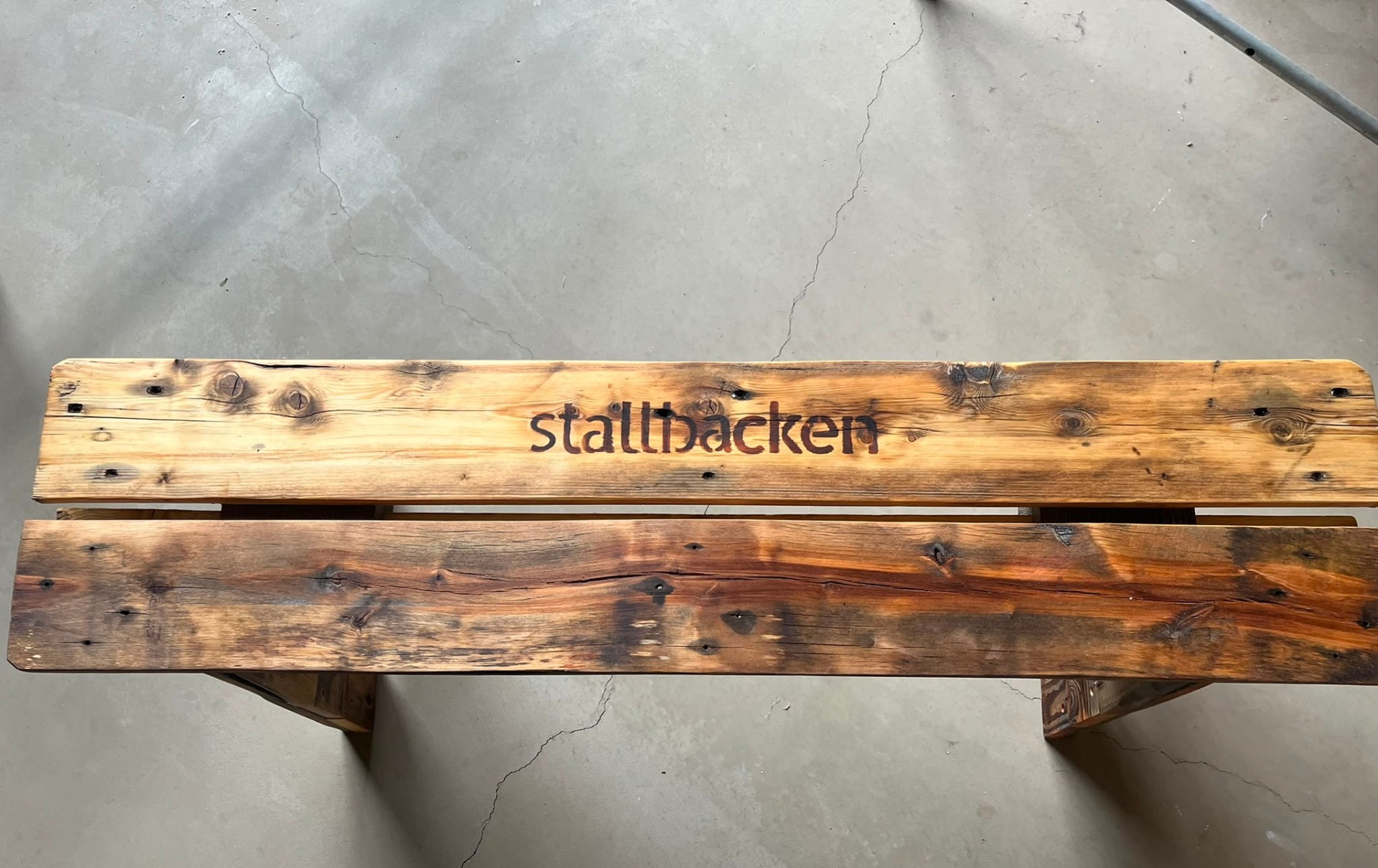 Närbild på inbränd text 'Stallbacken' på en pallbänk